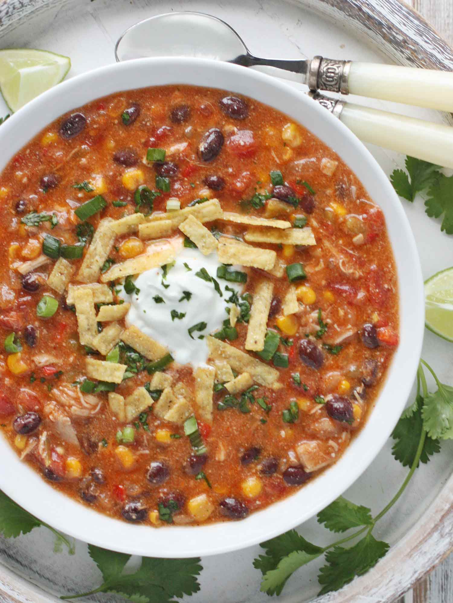 Zesty Chicken Enchilada Soup in a white bowl with spoons to the side.