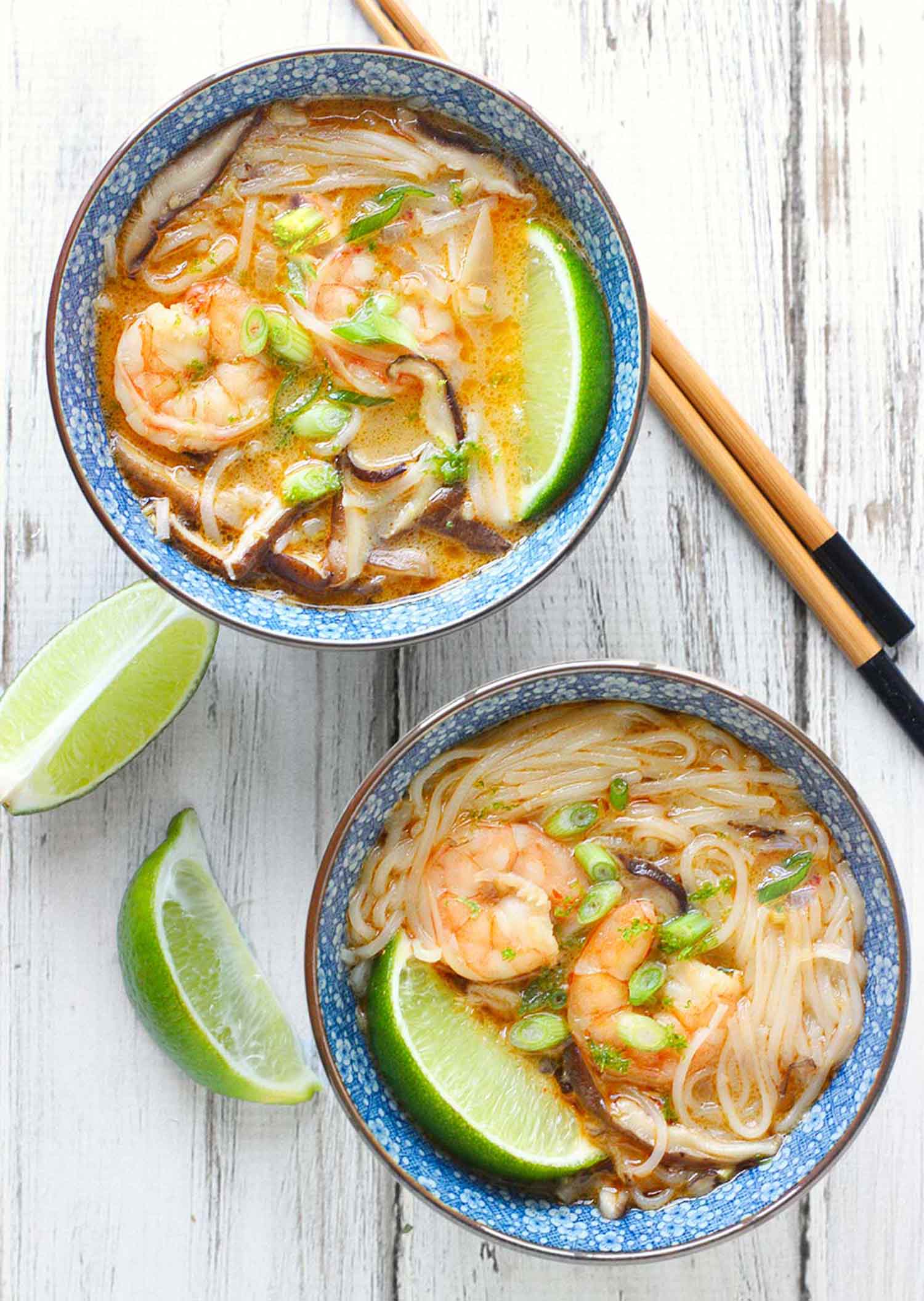 Overhead view of two bowls of Thai Curry Shrimp Soup with chopsticks and lime wedges on the side.
