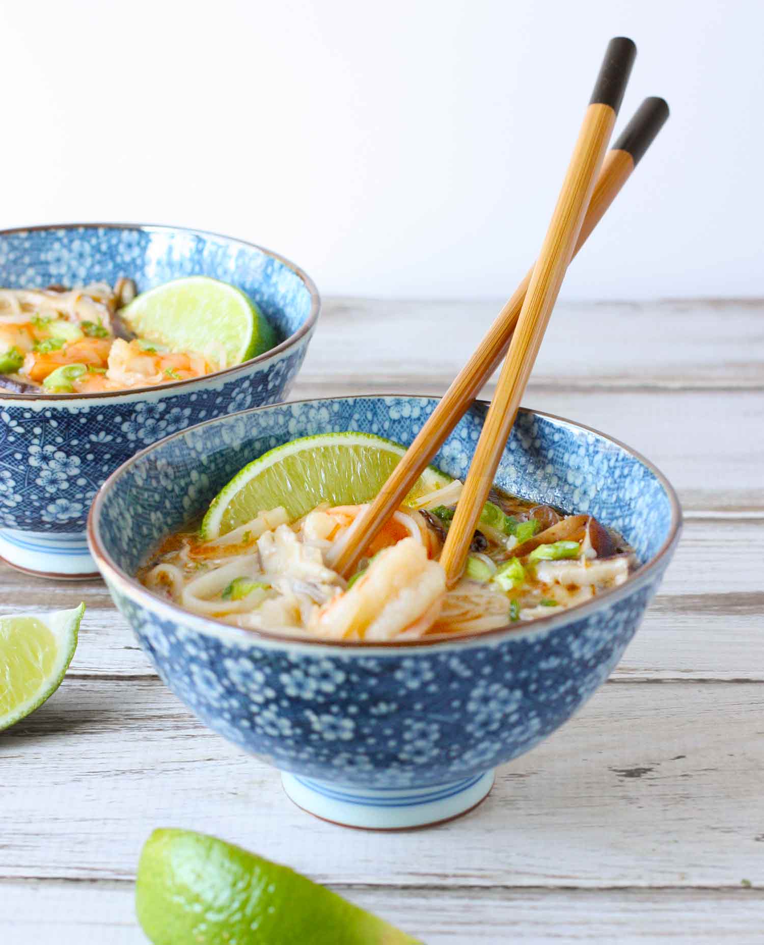 Side view of two bowls of Thai Curry Shrimp Soup with chopsticks.
