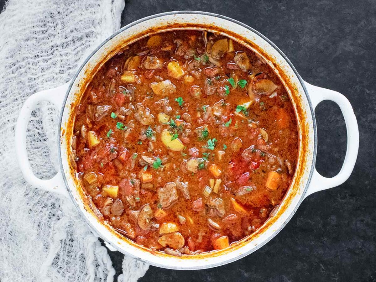 Braised Vegetable Beef Soup in a white Dutch oven, ready to serve.
