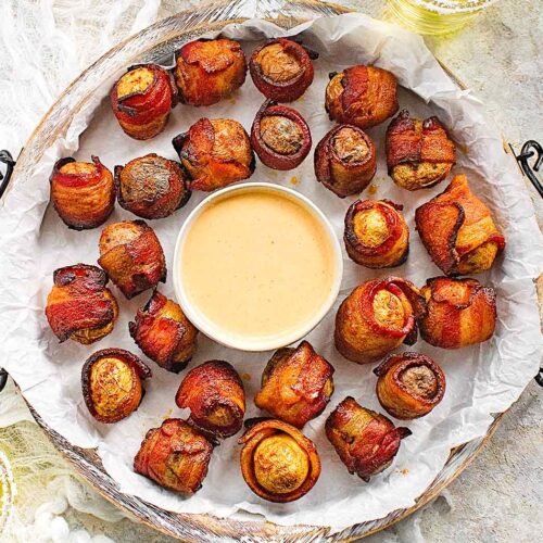 Bacon wrapped potato appetizers on a white serving tray with dip.
