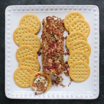 Cranberry Pecan Bacon Cheese Log on a white plate with crackers.