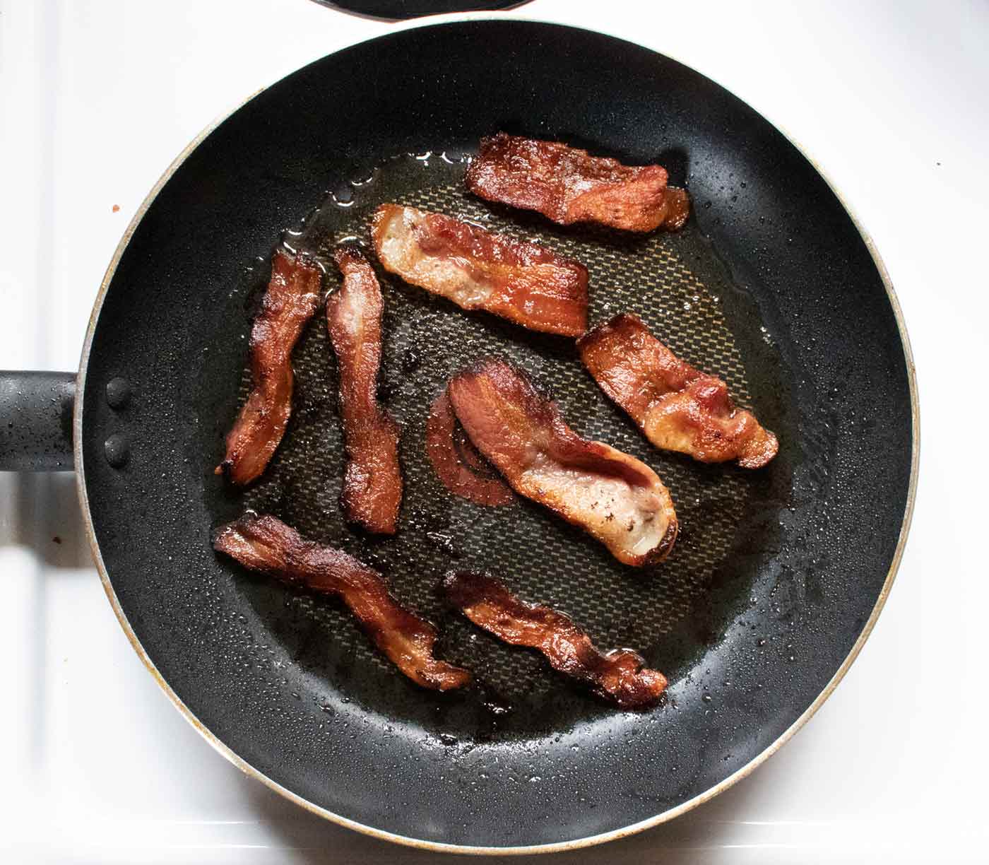 Step 1: Strips of bacon cooking in a skillet.