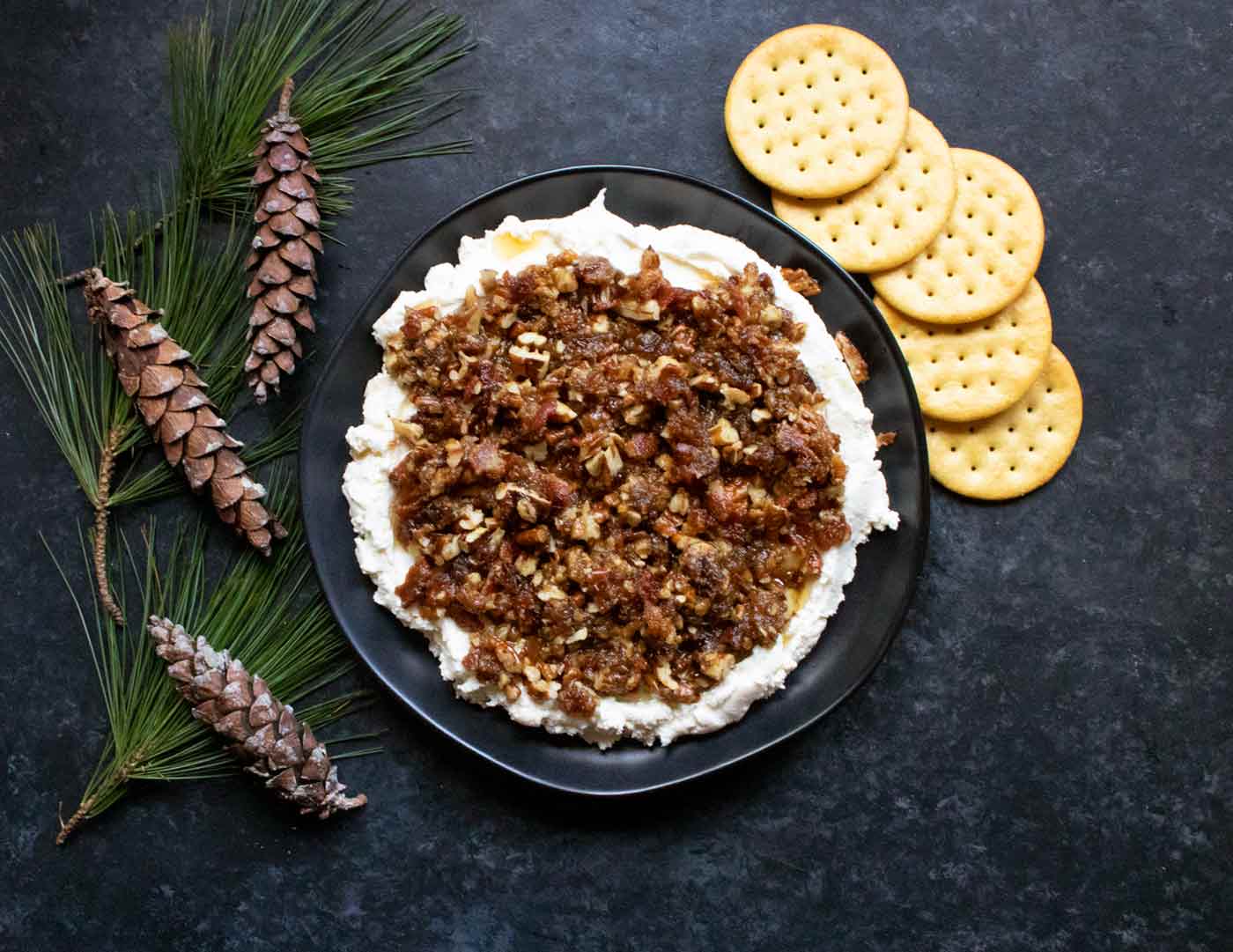 Creamy Goat Cheese Bacon and Dates Dip on a black plate with crackers.