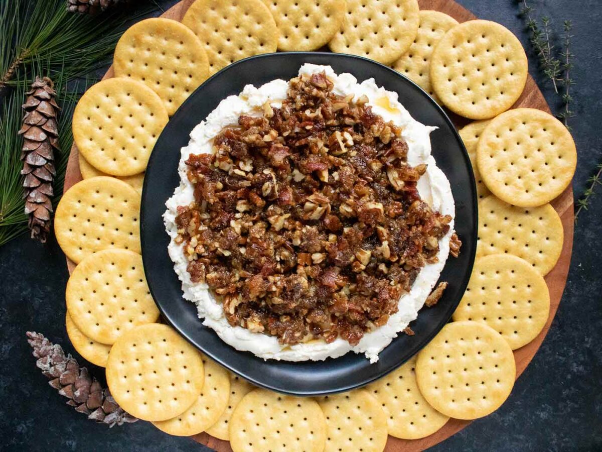 Creamy Goat Cheese Bacon and Dates Dip on a black plate, with crackers on a serving tray.