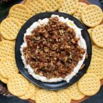 Creamy Goat Cheese Bacon and Dates Dip on a black plate, with crackers on a serving tray.