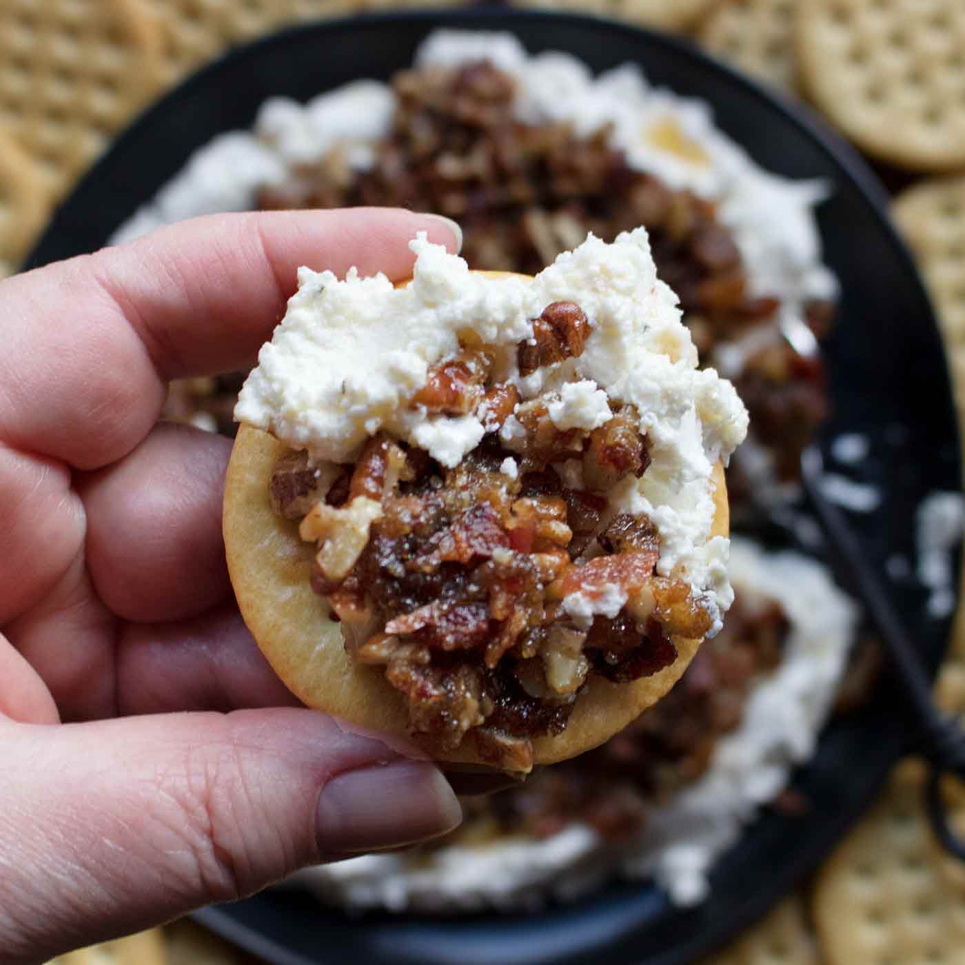 Close-up of Creamy Goat Cheese Bacon & Dates Dip spread on a cracker.