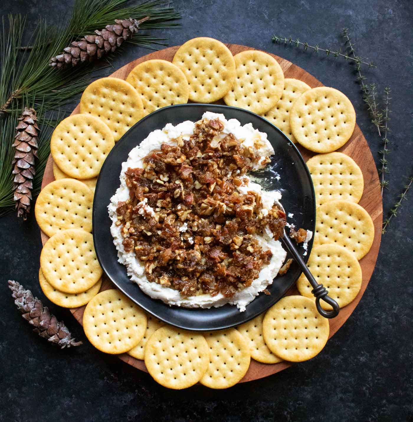 Creamy Goat Cheese Bacon and Dates Dip with crackers on a wooden serving board.