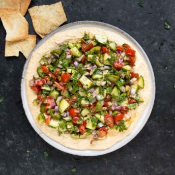 Layered Veggies & Hummus dip on a plate with chips on the side.
