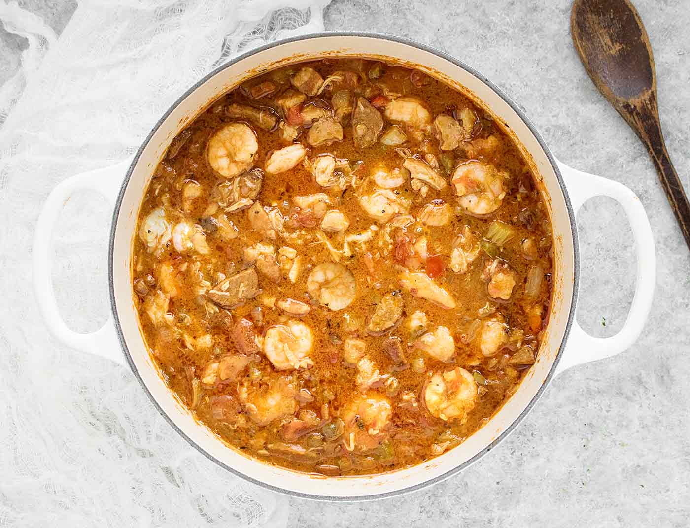 An overhead view of Chicken Seafood & Sausage Gumbo in a large white Dutch oven, ready to serve.