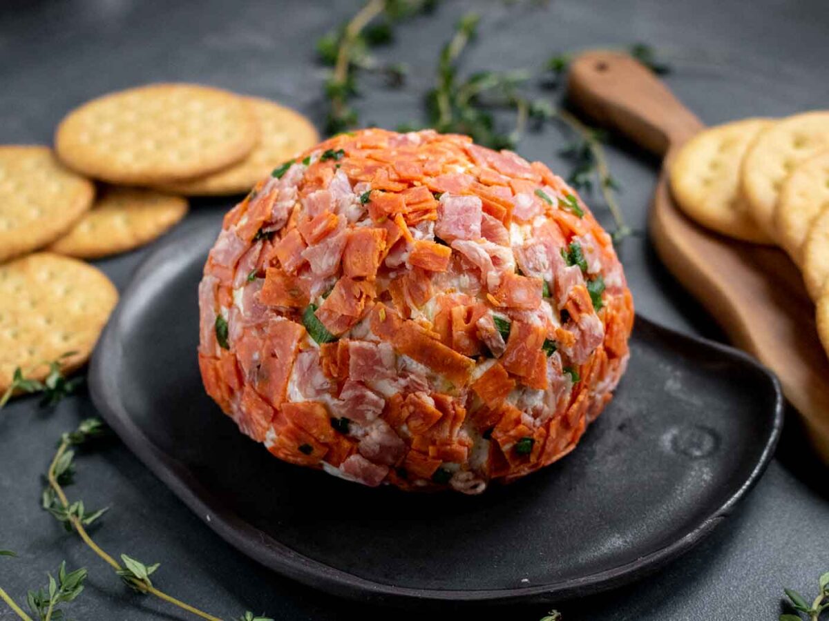 Side view of an Italian Grinder Cheese Ball on a black plate with crackers.