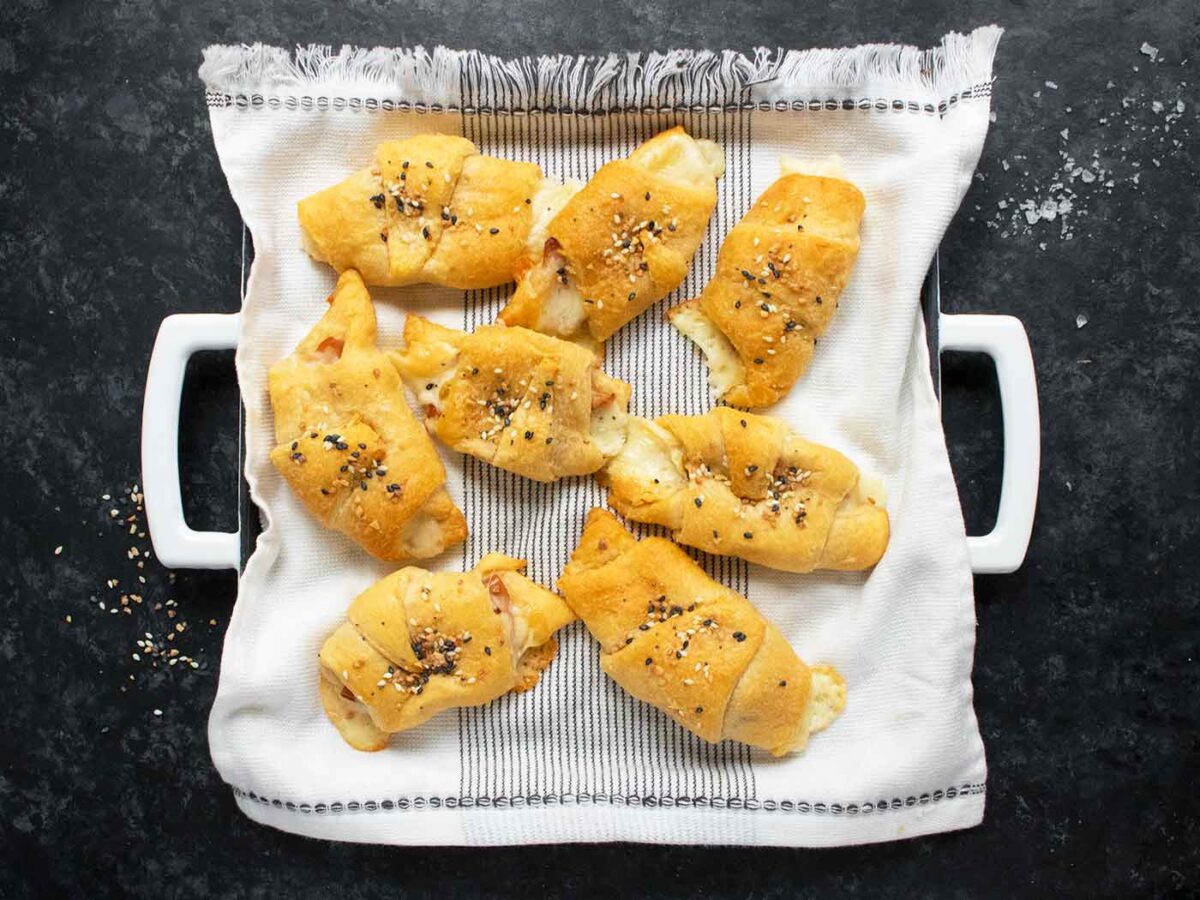 Overhead view of a platter of Mortadella Stuffed Crescent Rolls, nestled in a white towel with black stripes.