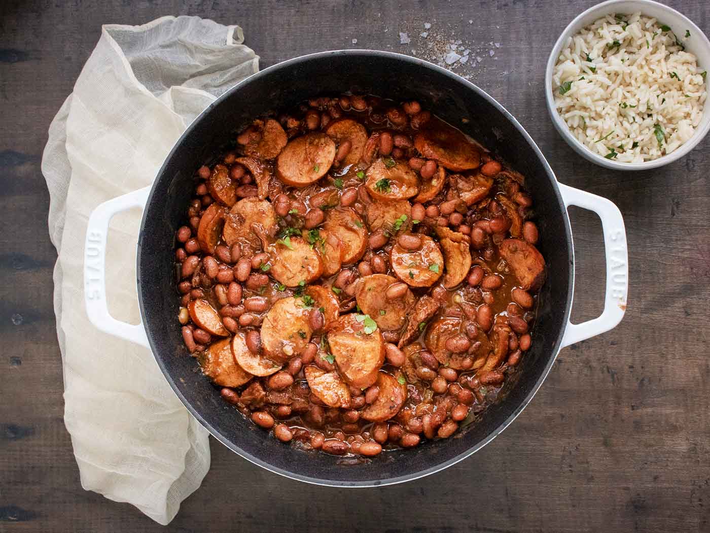 Overhead view of red beans and andouille sausage in a pot, with a side of rice.