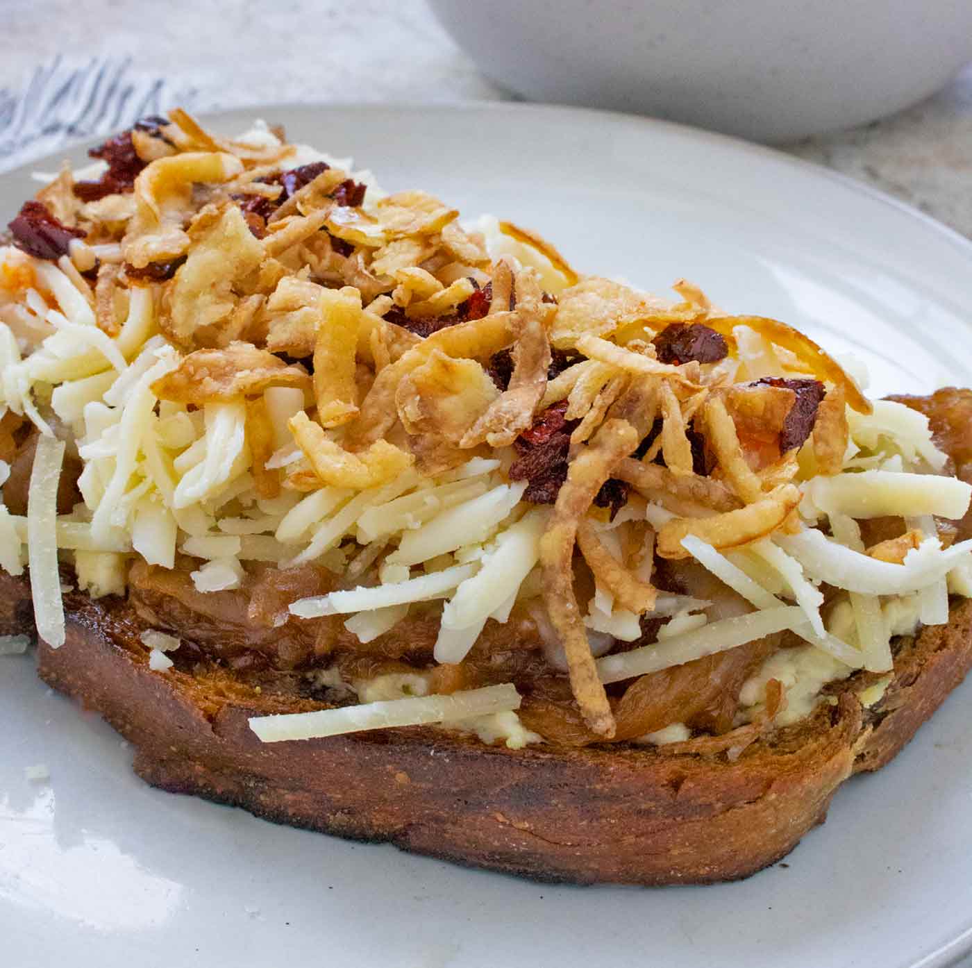 Side view of a Cheesy French Onion Fried Toast open-faced sandwich on a plate.