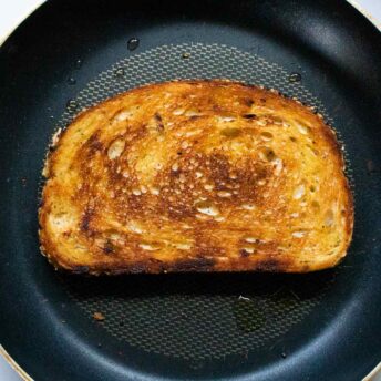 A slice of sourdough bread in a skillet, fried to a beautiful golden crispness.