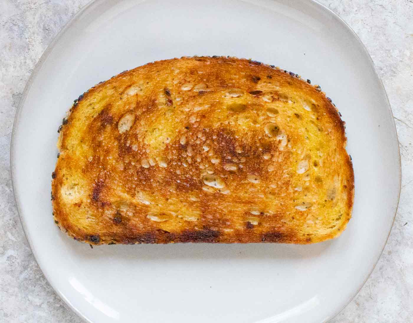 A slice of sourdough bread that's been fried until beautifully golden brown. It's sitting on a light gray plate, ready to enjoy.
