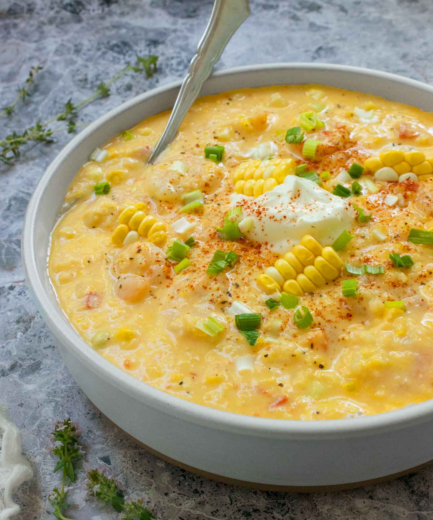 A side-angled view of a bowl of Shrimp and Corn Chowder, topped with green onions, rafts of corn kernels right off the cob, and a dollop of sour cream.