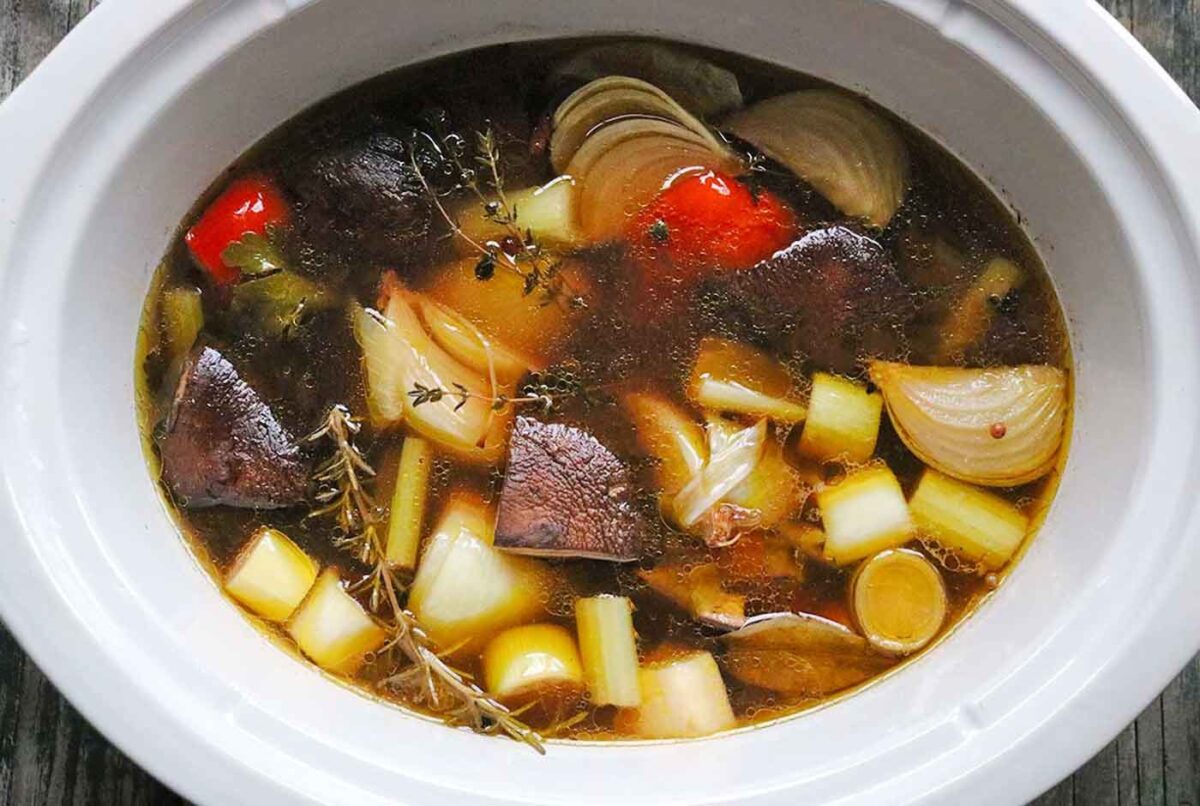 Overhead view of roasted vegetable stock in the pot of a slow cooker.