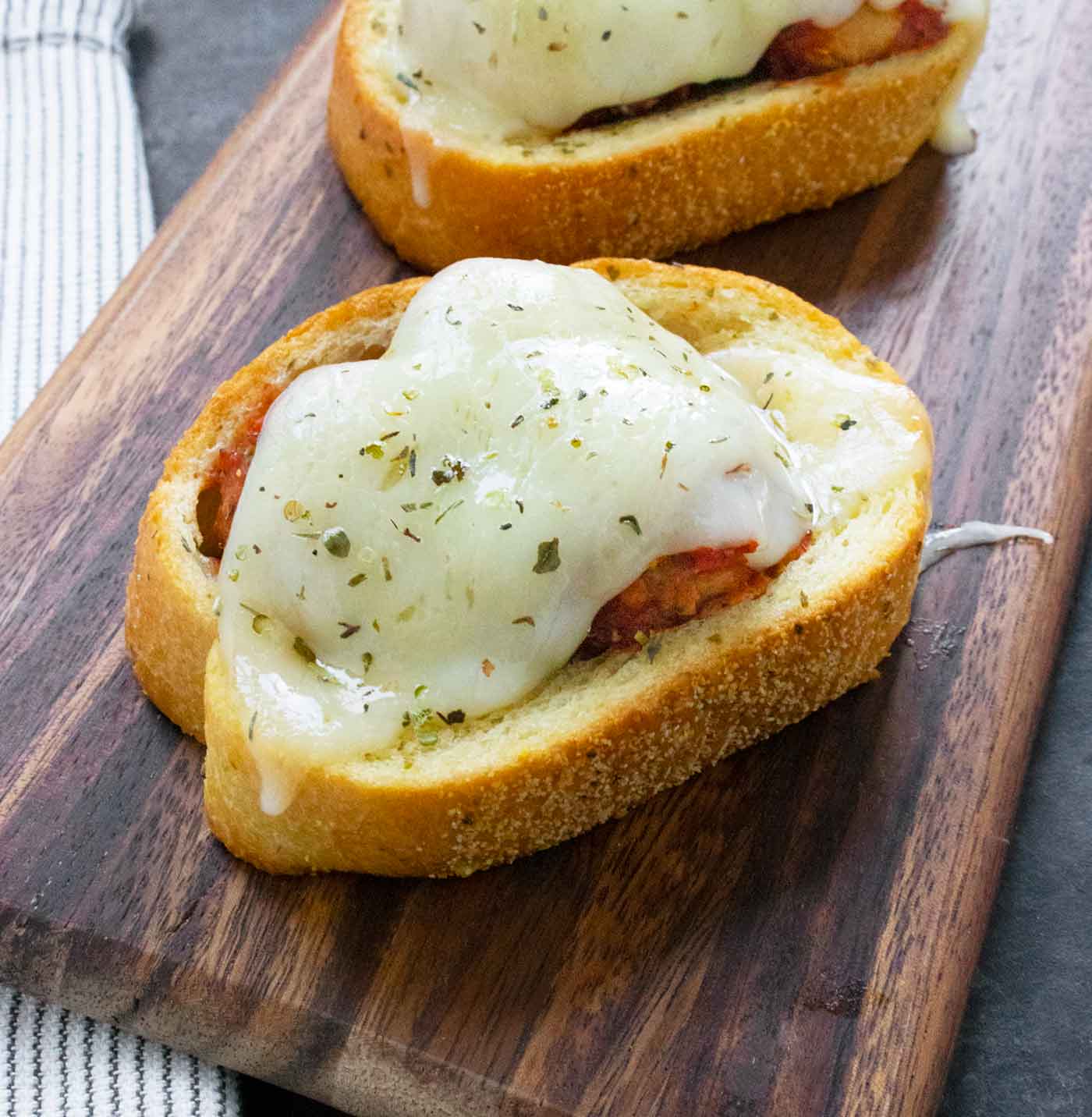 Two Meatballs on Texas Toast on a wooden serving board.