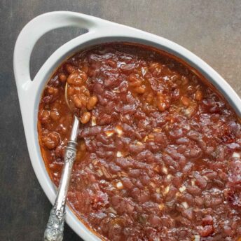 Overhead view of Oven-baked Canned Baked Beans in a white baking dish, with a spoon.