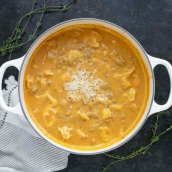 Overhead view of Creamy Pumpkin Sausage Tortellini Soup in a large white dutch oven.