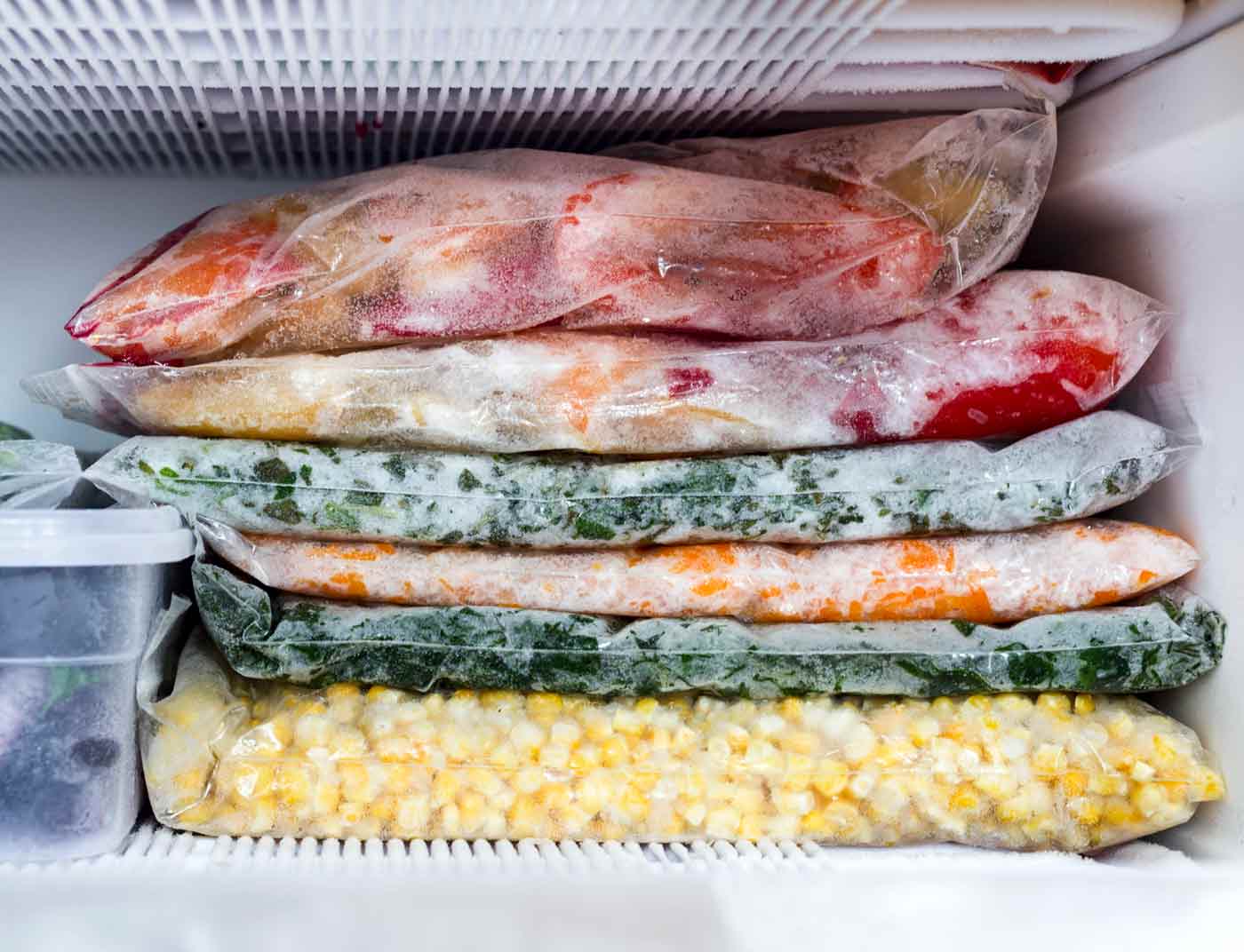 Food frozen flat in plastic bags, stacked on top of one another on the freezer shelf.