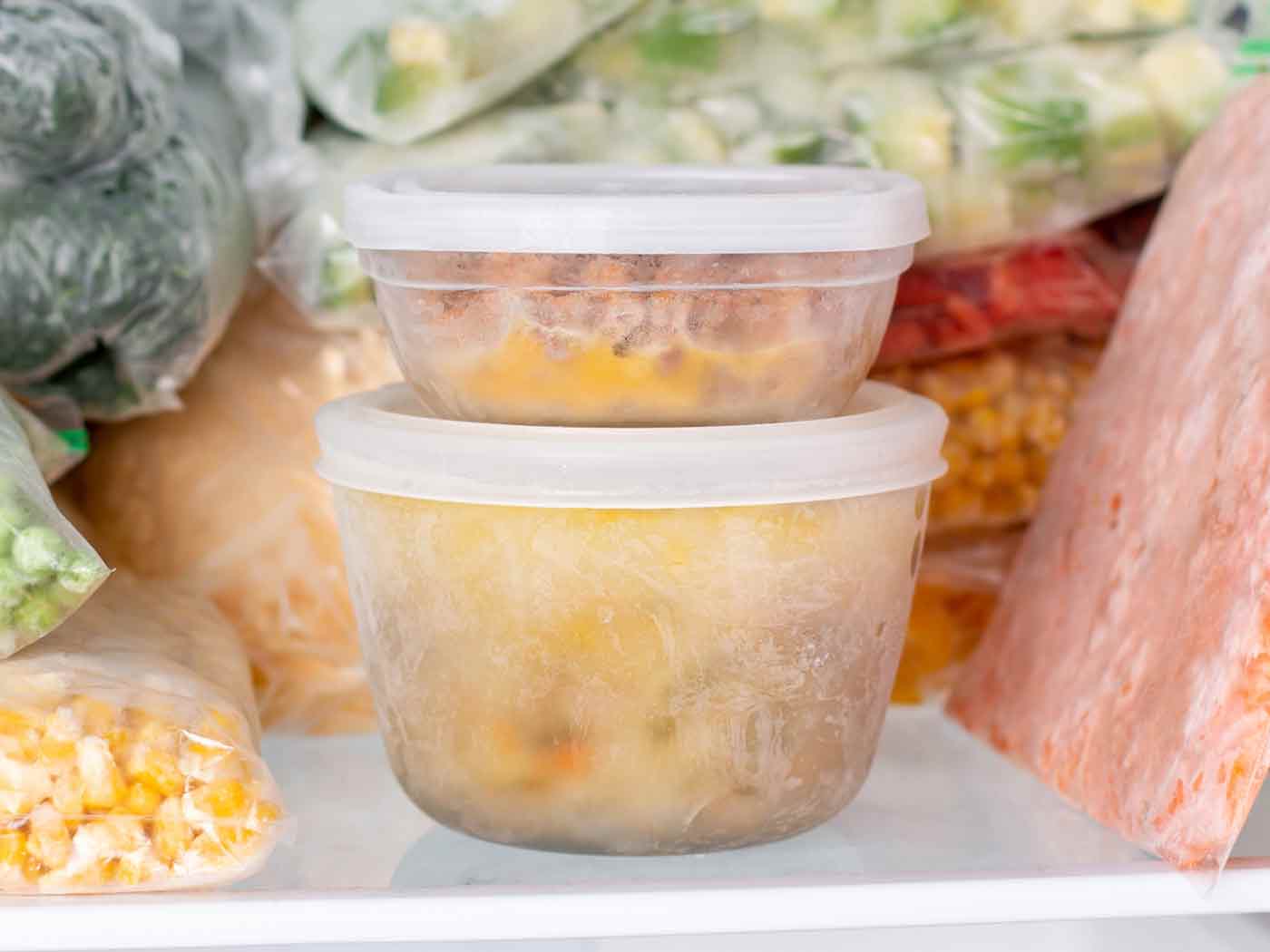 Soup frozen in containers, sitting on a freezer shelf with other foods.