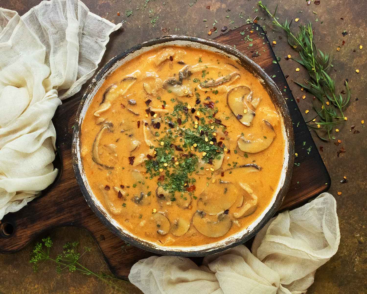 An overhead view of Thai Coconut Mushroom Soup in a rustic white bowl on a wooden serving board.