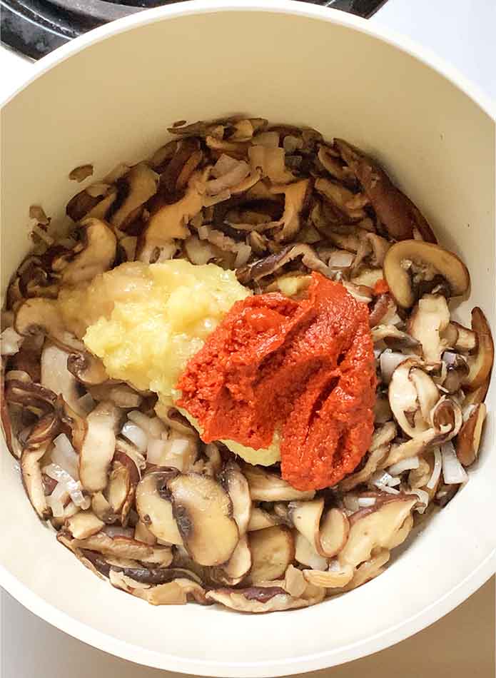Adding the ginger, lemongrass, garlic, and Thai red curry paste to the mushroom mixture.
