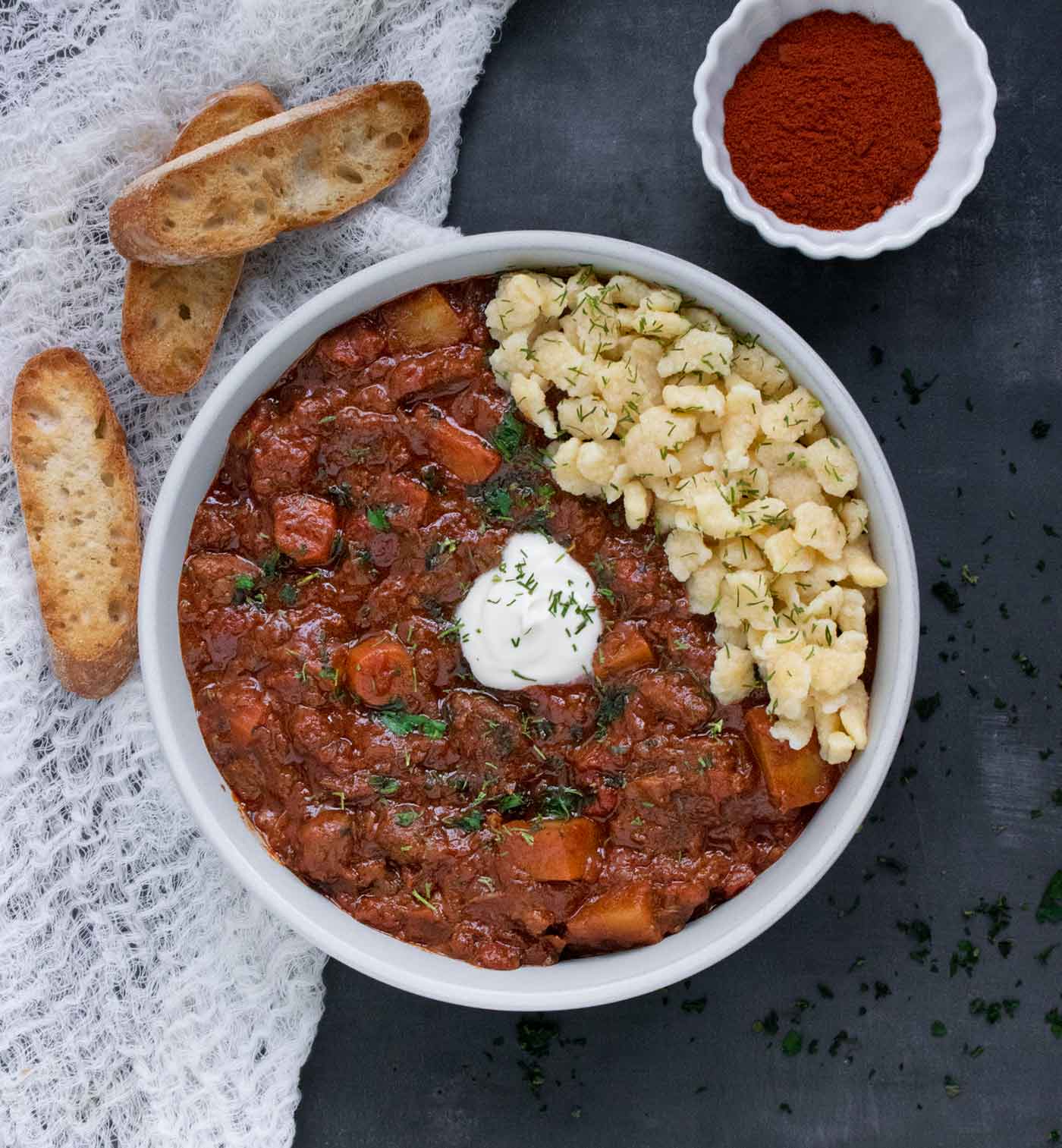 Overhead shot of a bowl of Austrian Hungarian Goulash with a side of bread.