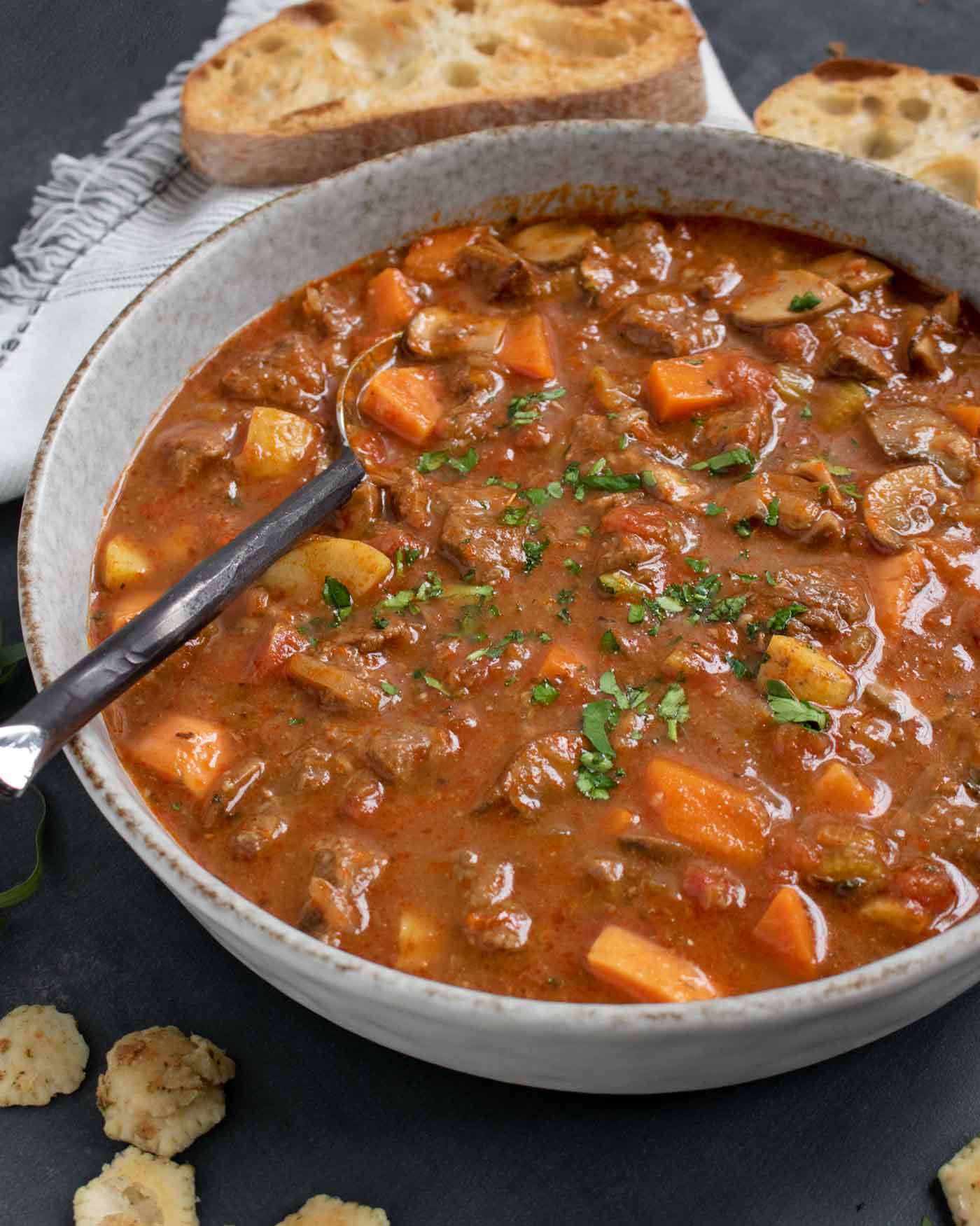 A side-angled view of a bowl of Braised Vegetable Beef Soup with a spoon.