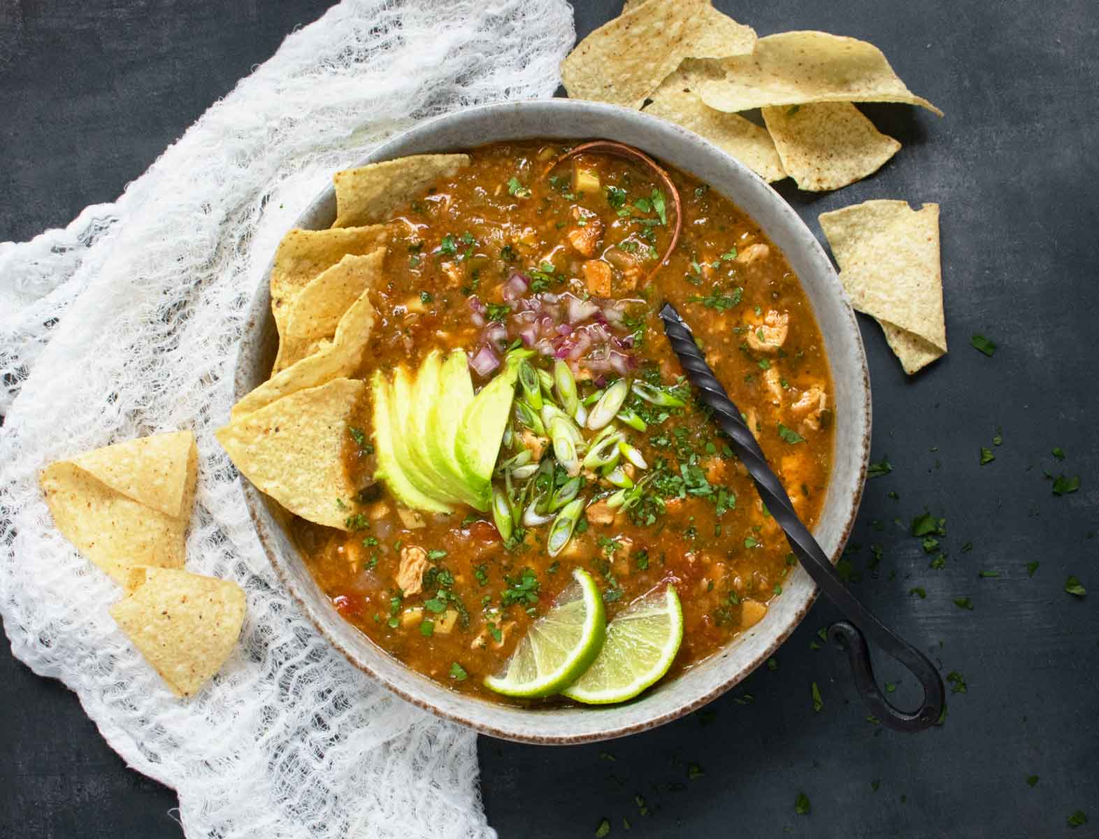 Overhead photo of Chile Verde Tortilla Soup in a bowl with a wrought iron spoon.