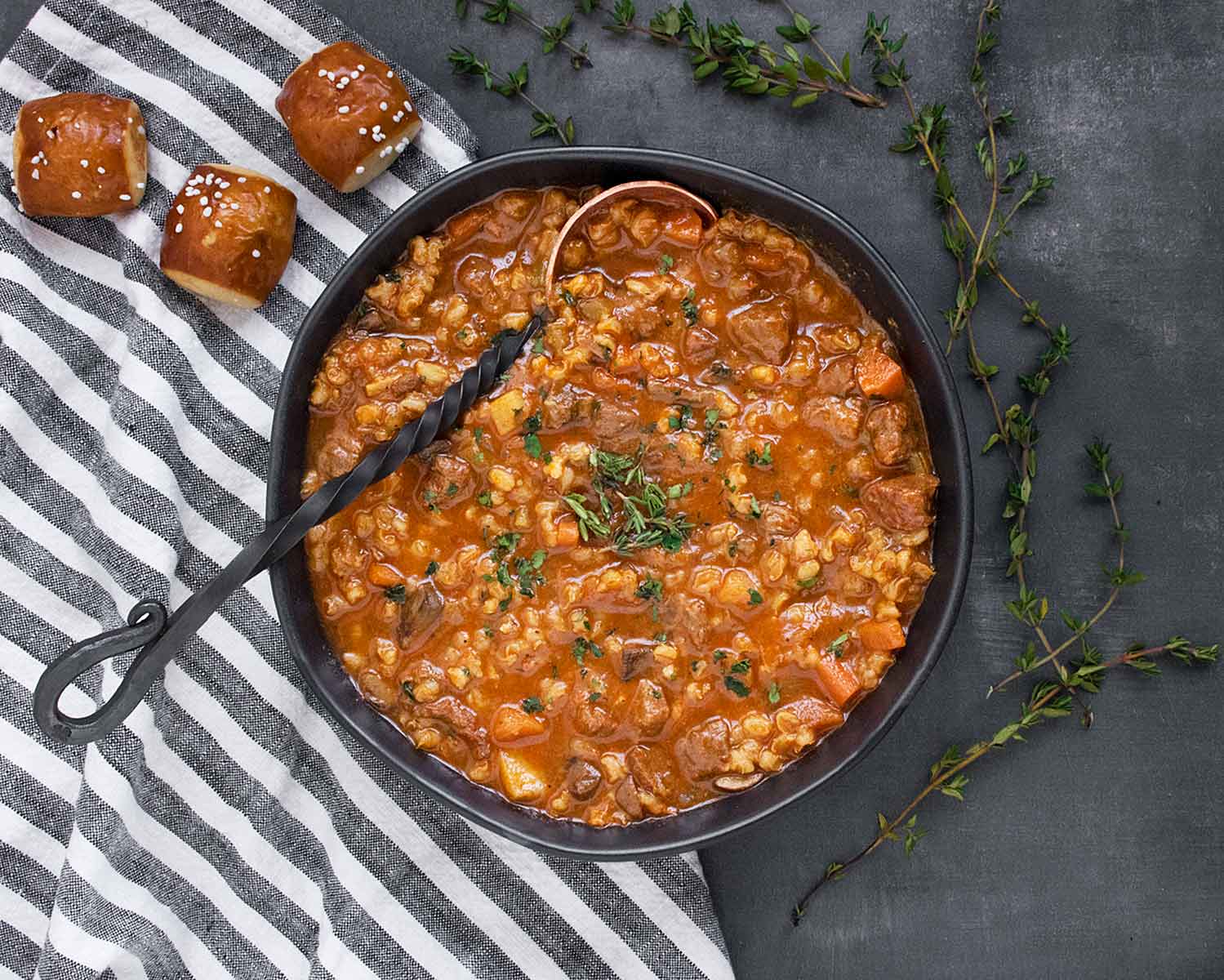 Overhead shot of Beef Barley Soup in a black bowl with a wrought iron spoon.