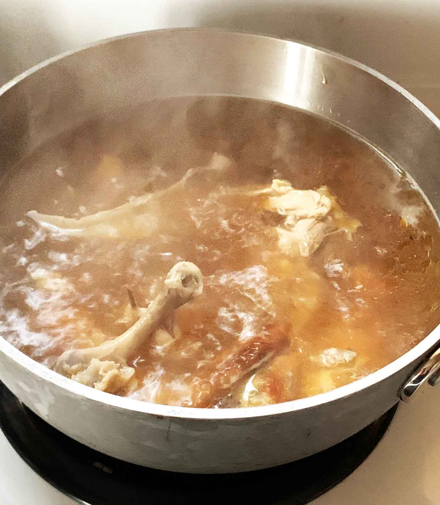 A pot of homemade chicken broth in the process of cooking.