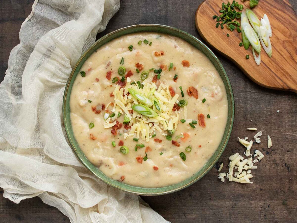 Overhead view of Irish Potato Soup in a green bowl, with a scattering of toppings on the side.