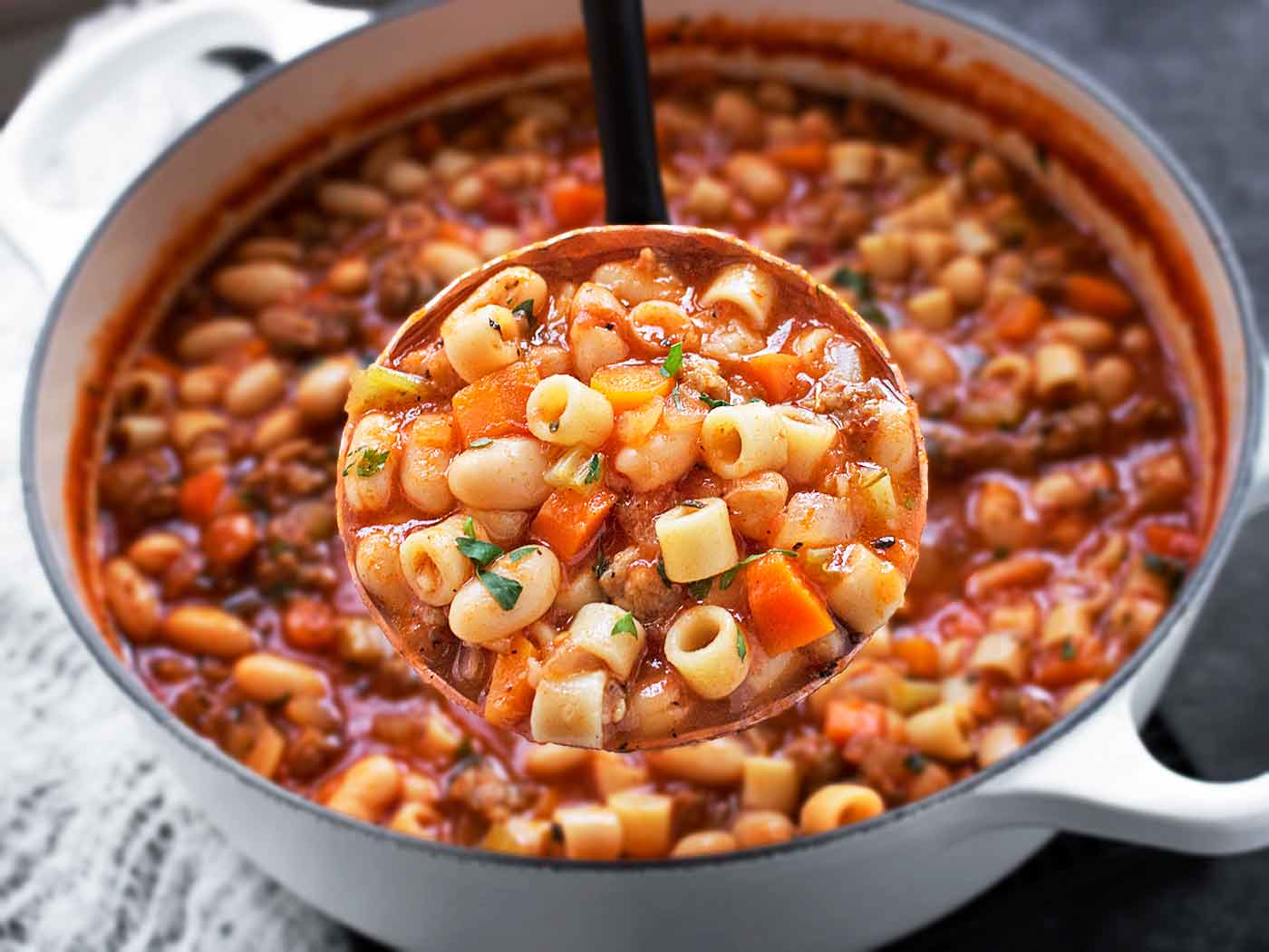 Close-up of a ladleful of Pasta e Fagioli soup, with the Dutch oven in the background.