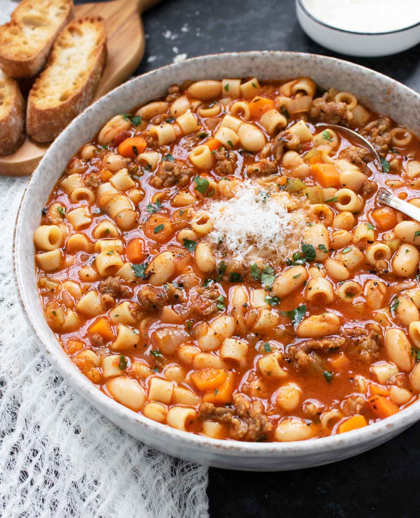 A side-angled view of Pasta e Fagioli in a speckled gray bowl with a side of sliced bread.