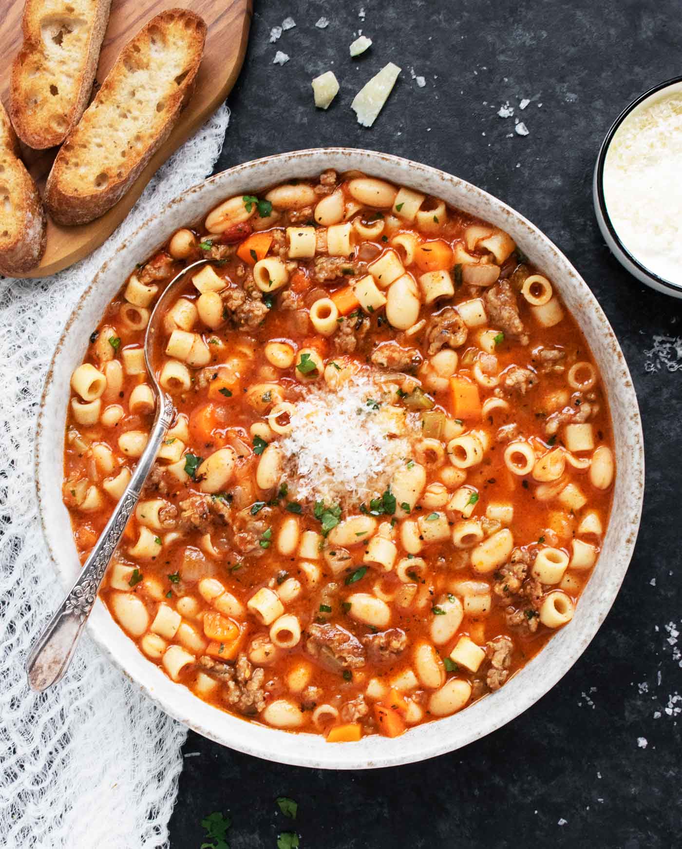 Overhead view of a bowl of Pasta e Fagioli with a spoon, and a side of bread.