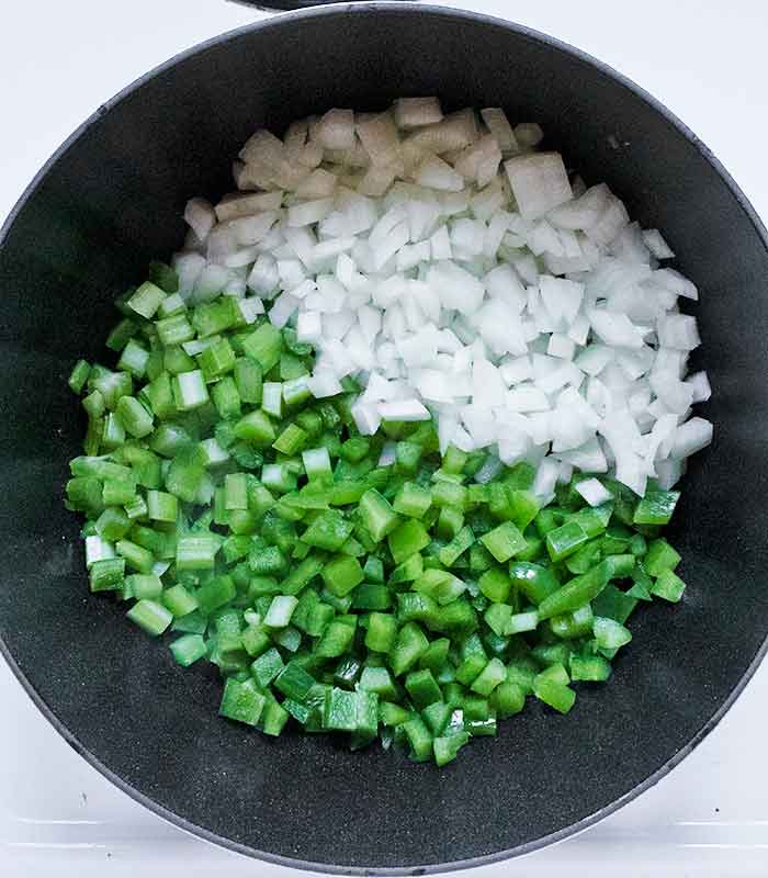 Onions, green bell peppers, and celery (clockwise) in the pot, ready to cook.