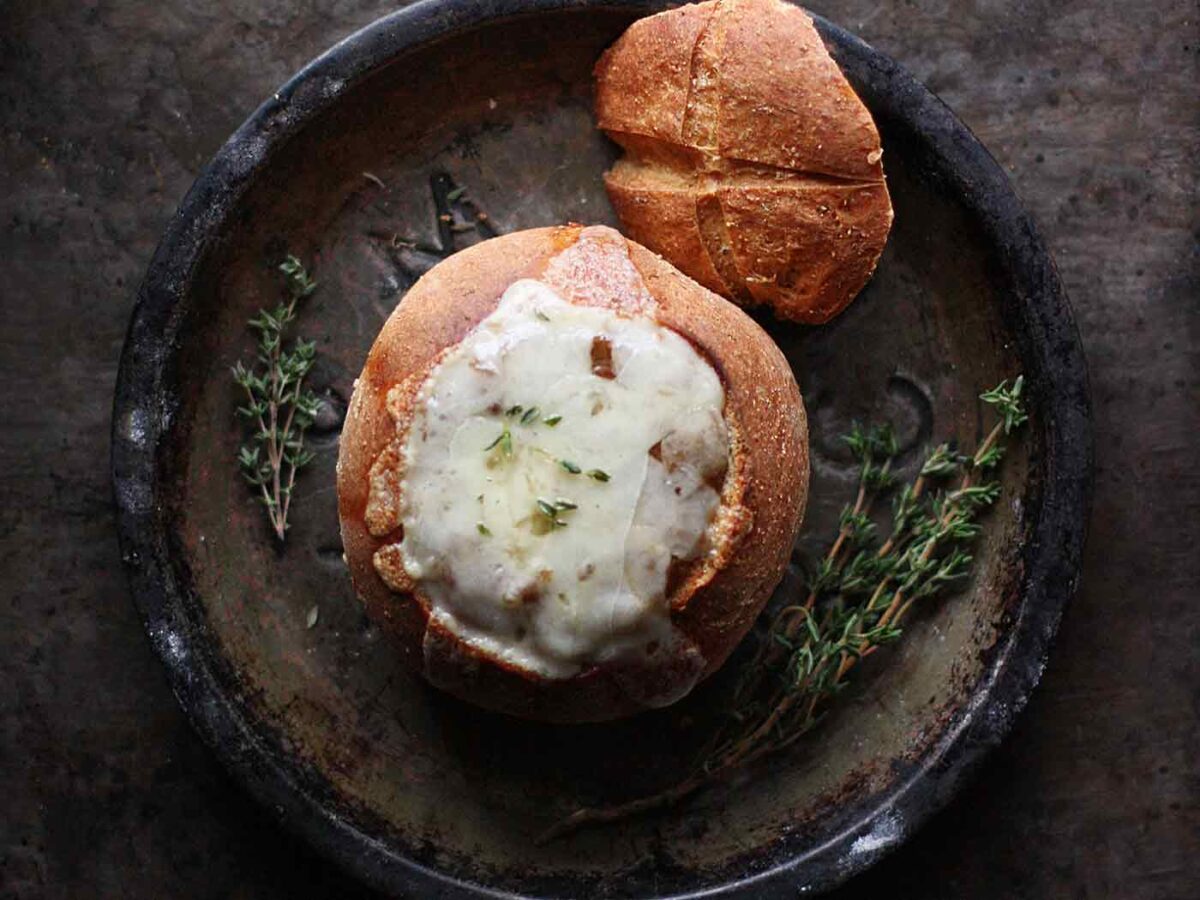 Overhead view of Vegetarian French Onion Soup in a bread bowl on a tin plate.