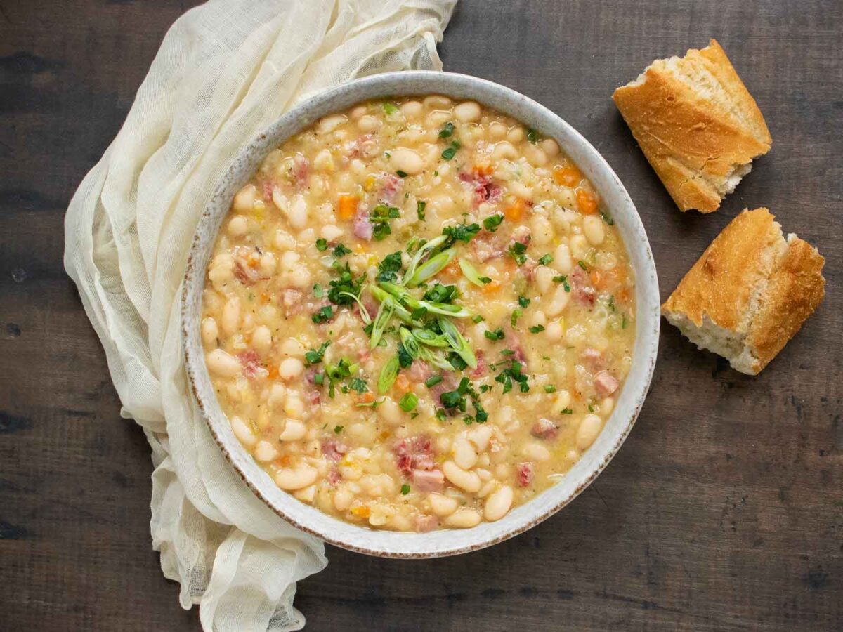 Ham and Bean Soup in a white bowl with a side of bread.