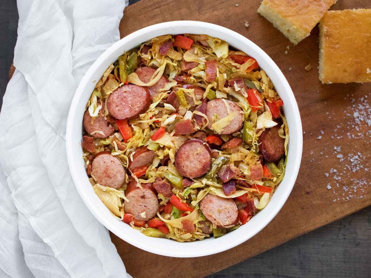 A bowl of Southern Fried Cabbage on a wooden serving board with cornbread.