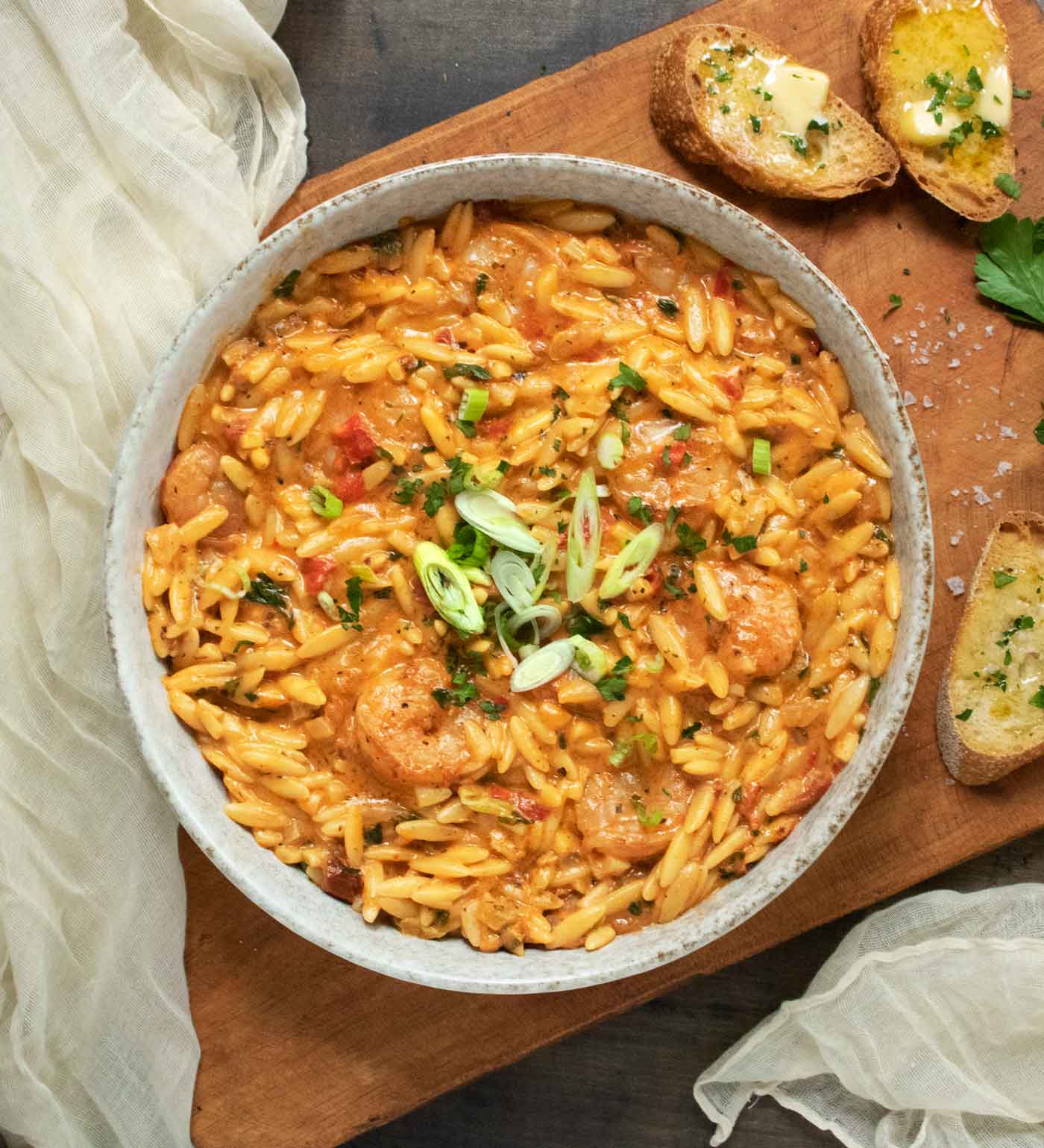 A bowl of Marry Me Shrimp & Orzo on a wooden board with buttered bread on the side.