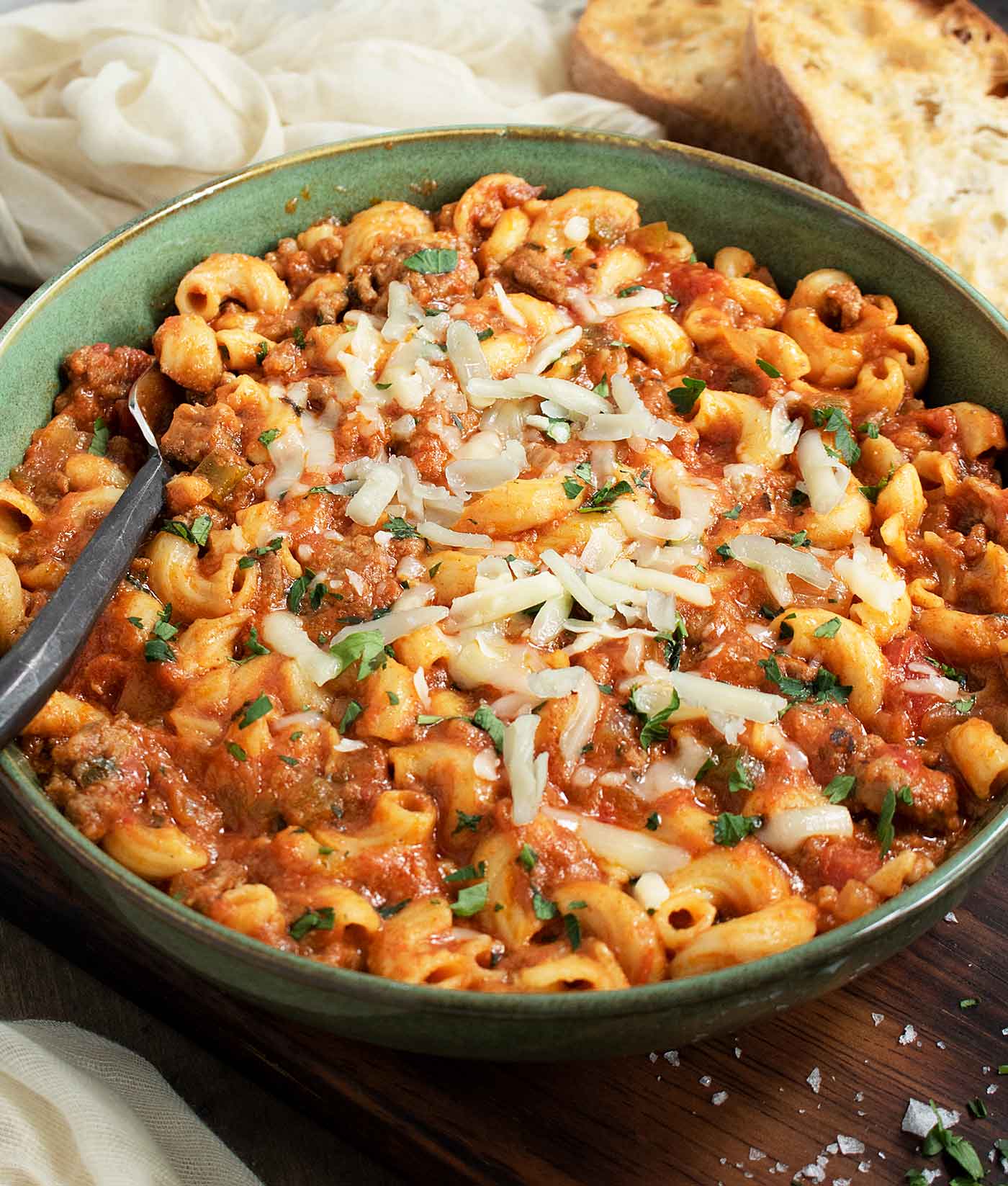 Side-angled view of American Goulash in a green bowl with a fork.