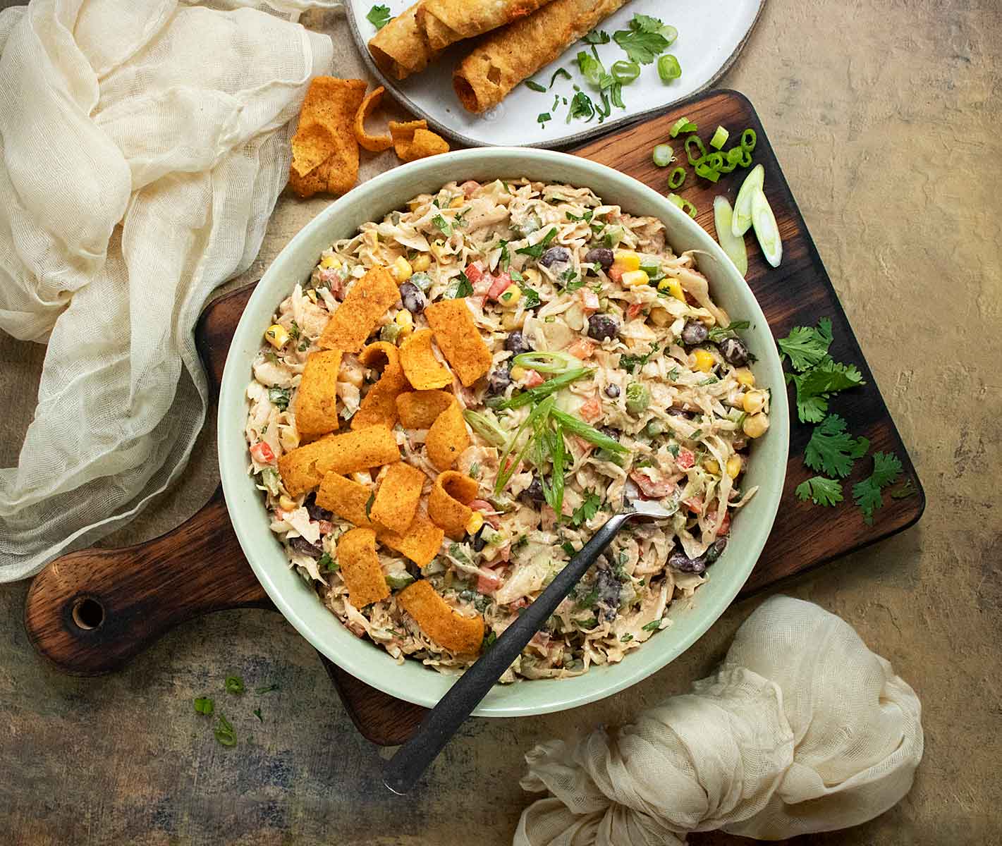 Cowboy Coleslaw with Fritos in a light green bowl with a fork on a serving board.