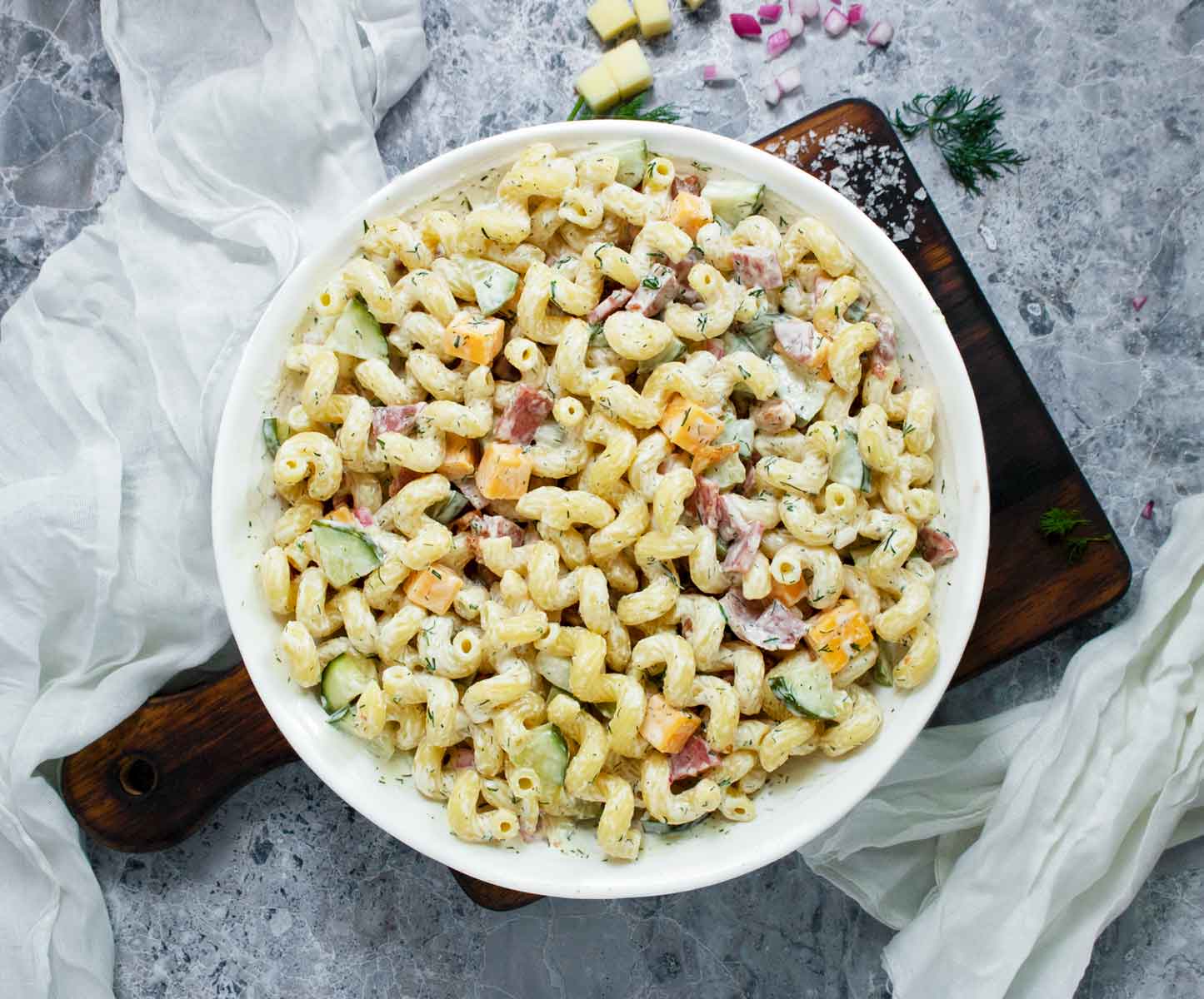 Dill Pickle Pasta Salad in a white bowl on a wooden serving board.
