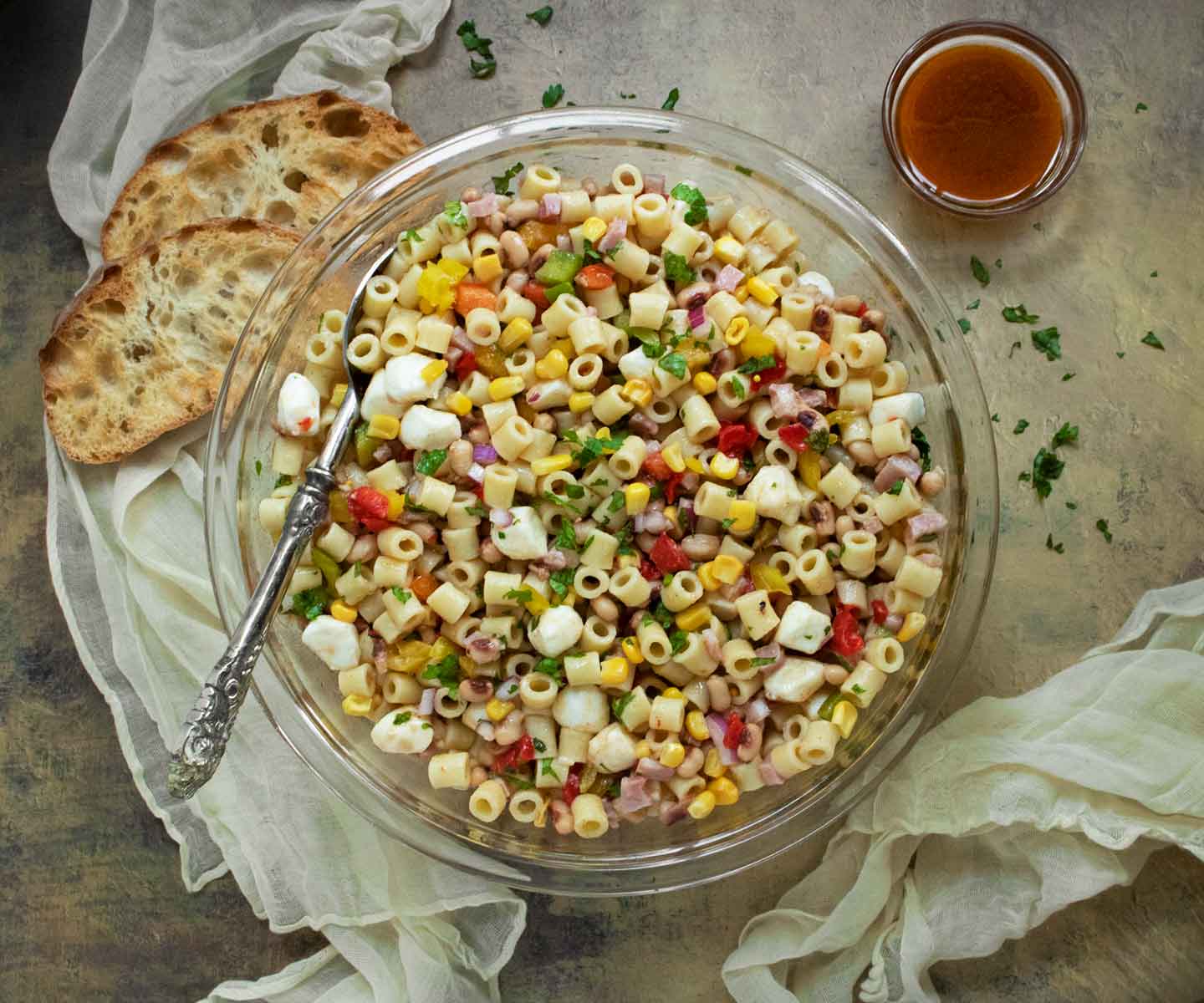 Overhead view of Cowboy Caviar Pasta Salad in a glass serving bowl with a side of bread slices.