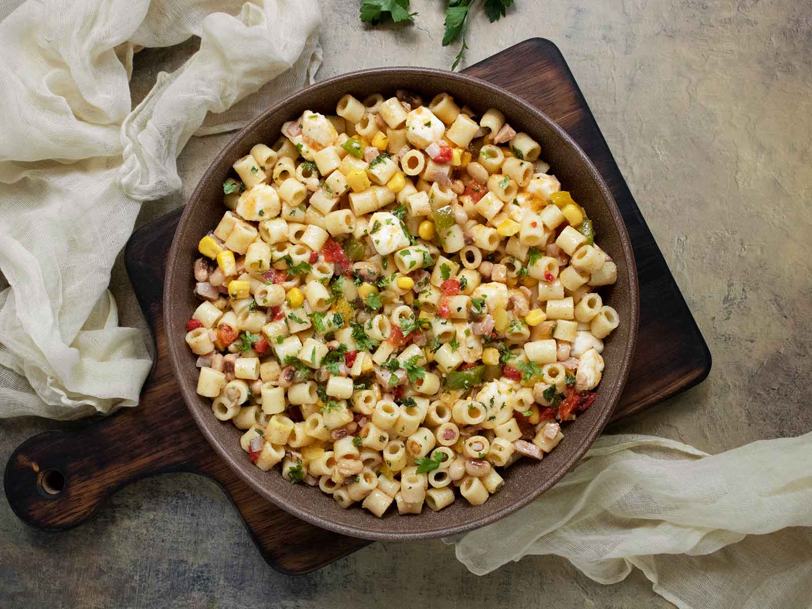 Cowboy Caviar Pasta Salad in a dark brown bowl on a wooden serving board.