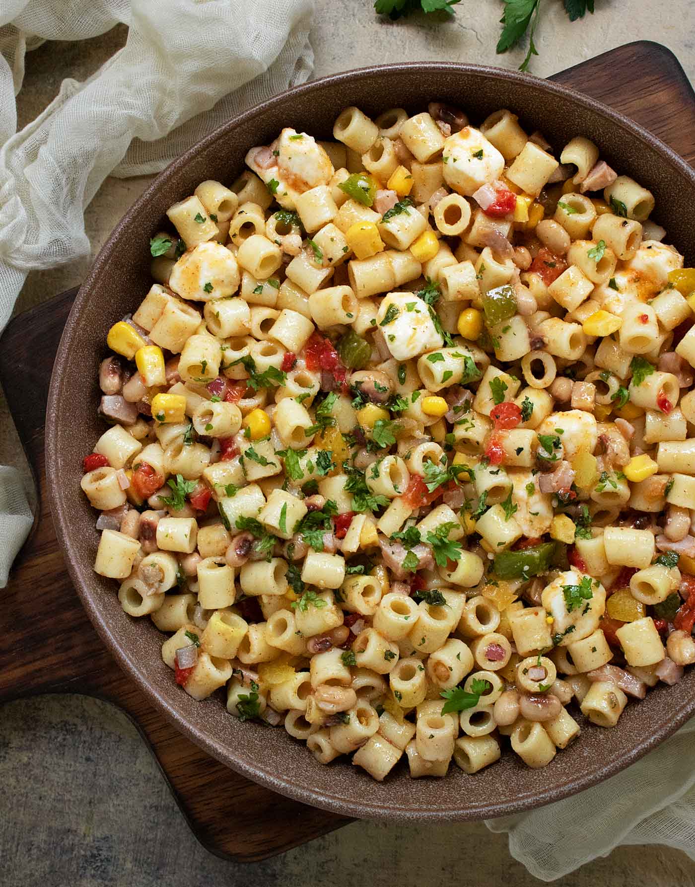 Cowboy Caviar Pasta Salad in a dark, clay-colored bowl on a wooden serving board.