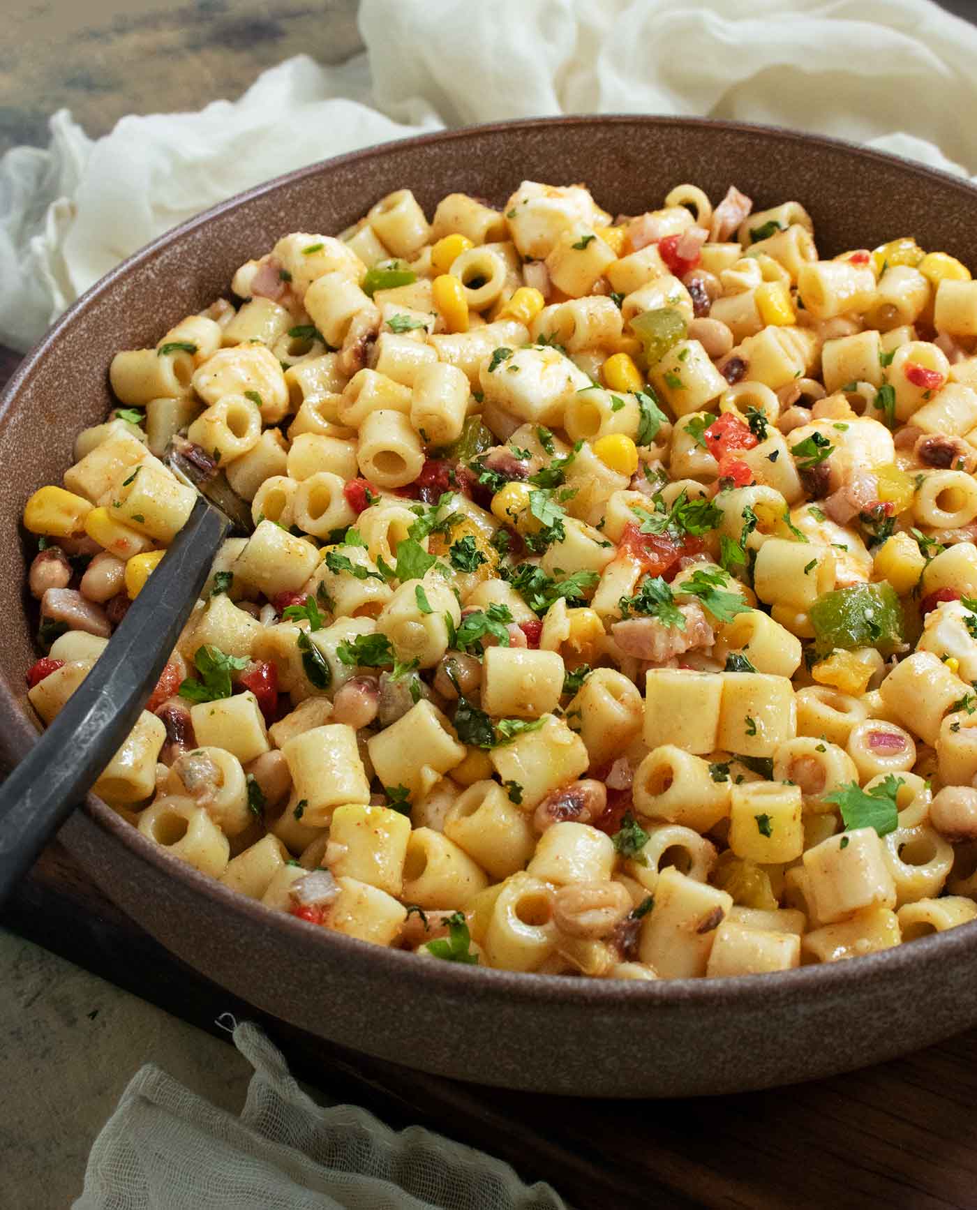 A side-angled view of Cowboy Caviar Pasta Salad in a large clear glass serving bowl, with a serving spoon.